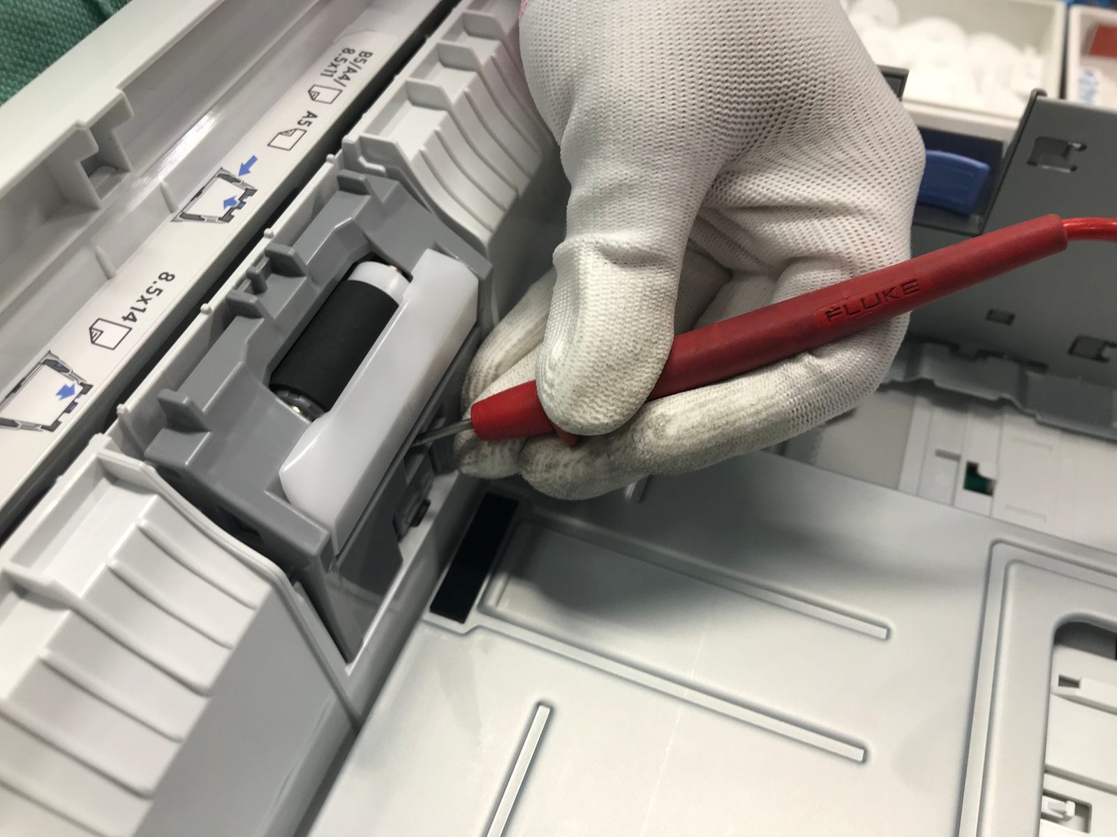 Technician servicing the paper feed rollers inside an office printer during refurbishment